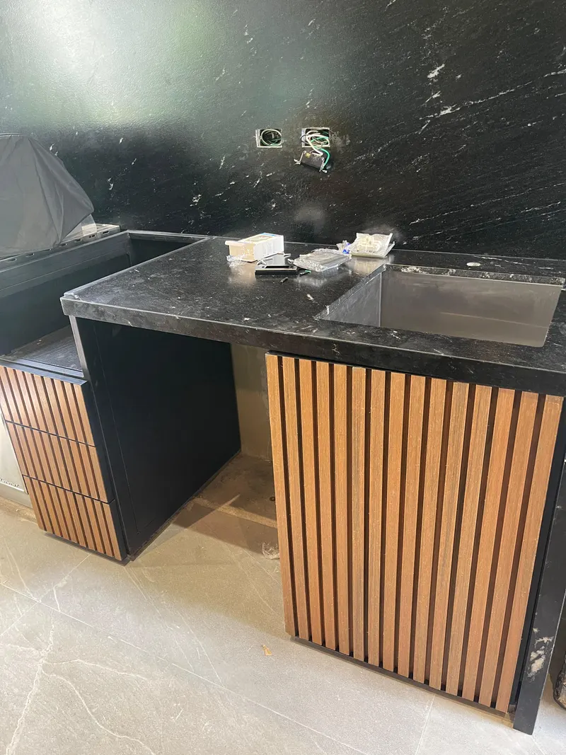 Cubierta negra con tarja y, debajo, puertas de tablillas verticales con apariencia de madera sobre marco oscuro