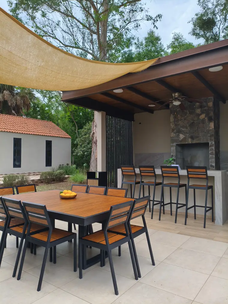 Comedor de exterior con cubierta color maple y sillas, junto a una barra con bancos altos, en una terraza techada