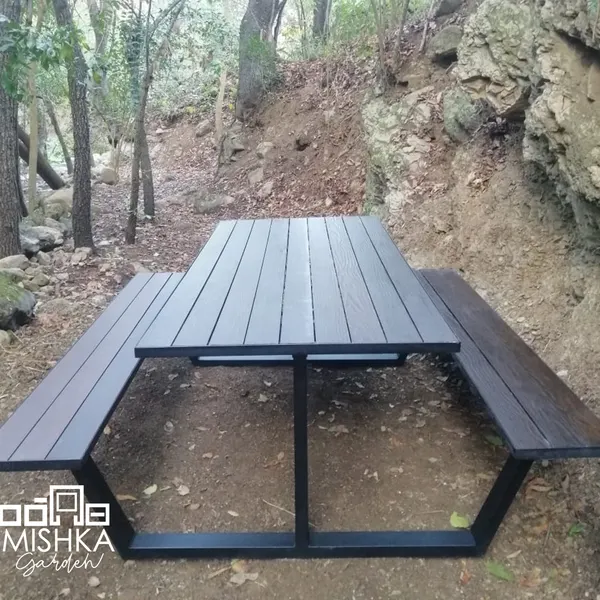 Mesa tipo picnic con sus bancas, vista desde un extremo, en un terreno con árboles