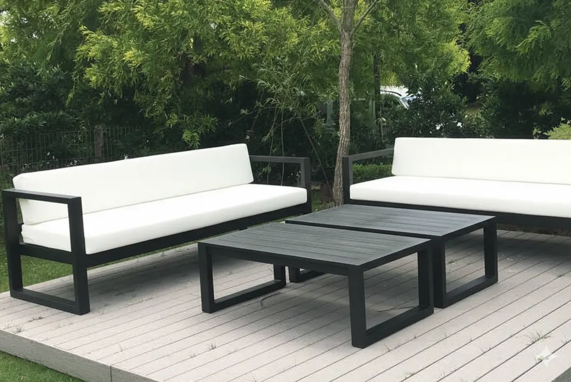 Sala de exterior en una terraza: dos sillones largos de estructura oscura con cojines blancos y dos mesas de centro, con árboles al fondo