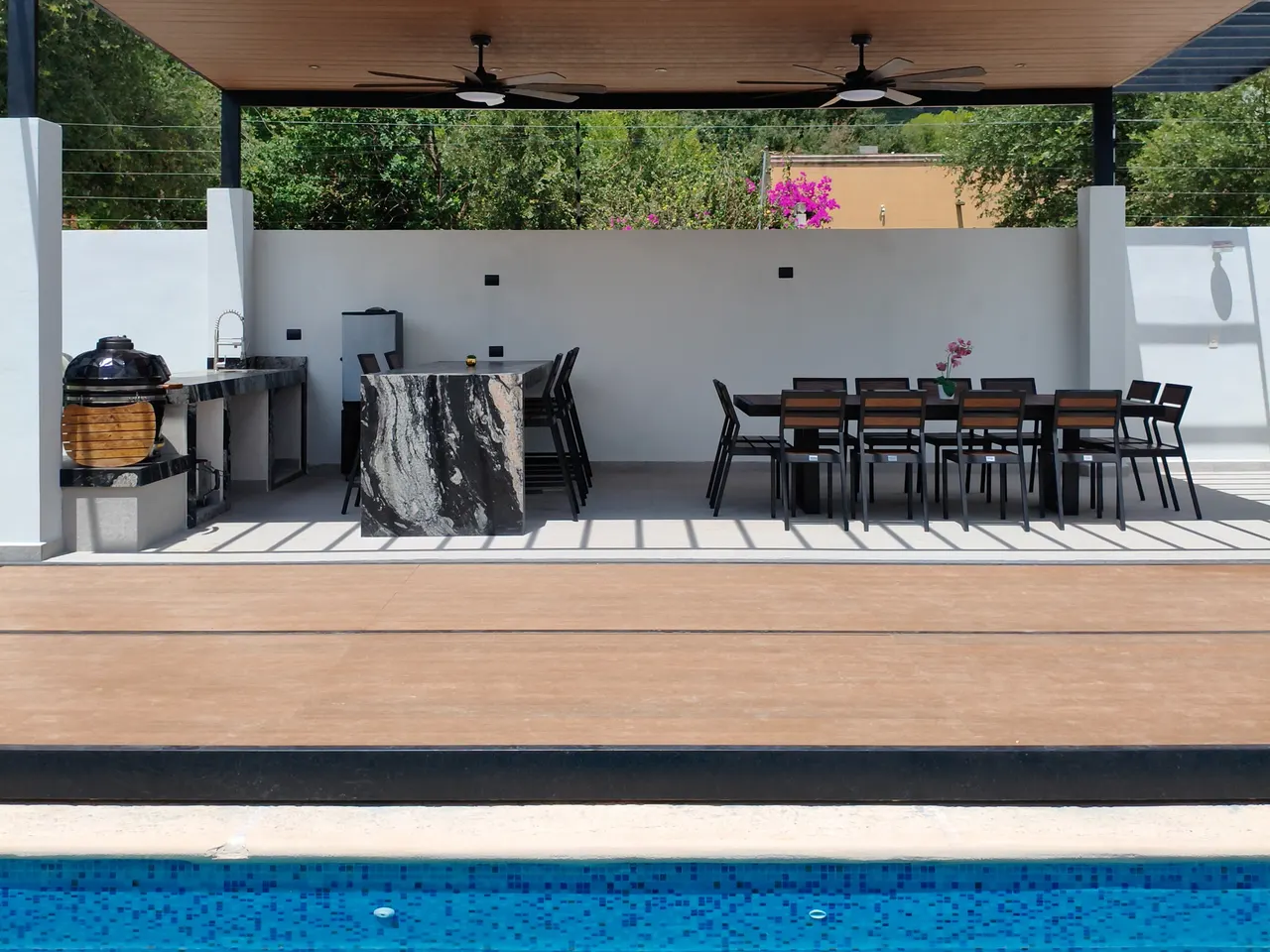 Terraza con pérgola, isla de cocina, asador redondo y un comedor largo con doce sillas